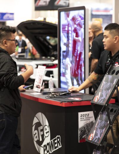 Man standing at host stand greeting people at aFe POWER booth at SEMA 2022 Las Vegas Car Show