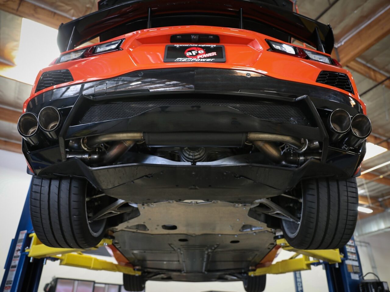 Underneath view of 2020 Bright Orange C8 Corvette lifted on car lift to show aFe POWER Exhaust system