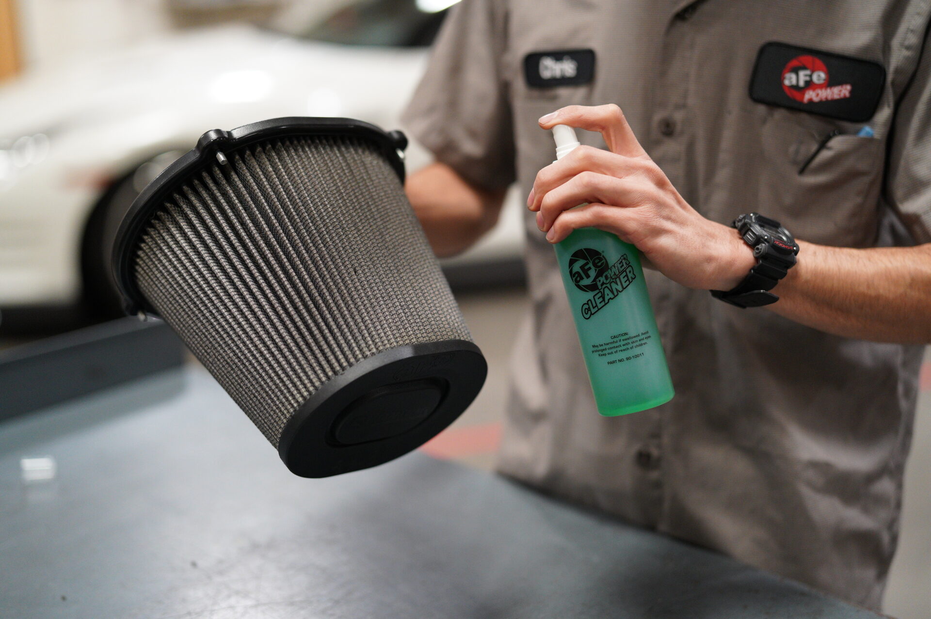 Man spraying aFe filter cleaner onto a grey engine air filter