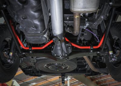 Shot underneath 2022 Toyota Tundra Truck showing aftermarket aFe POWER exhaust and aftermarked aFe CONTROL bright red rear sway bars in mechanic shop