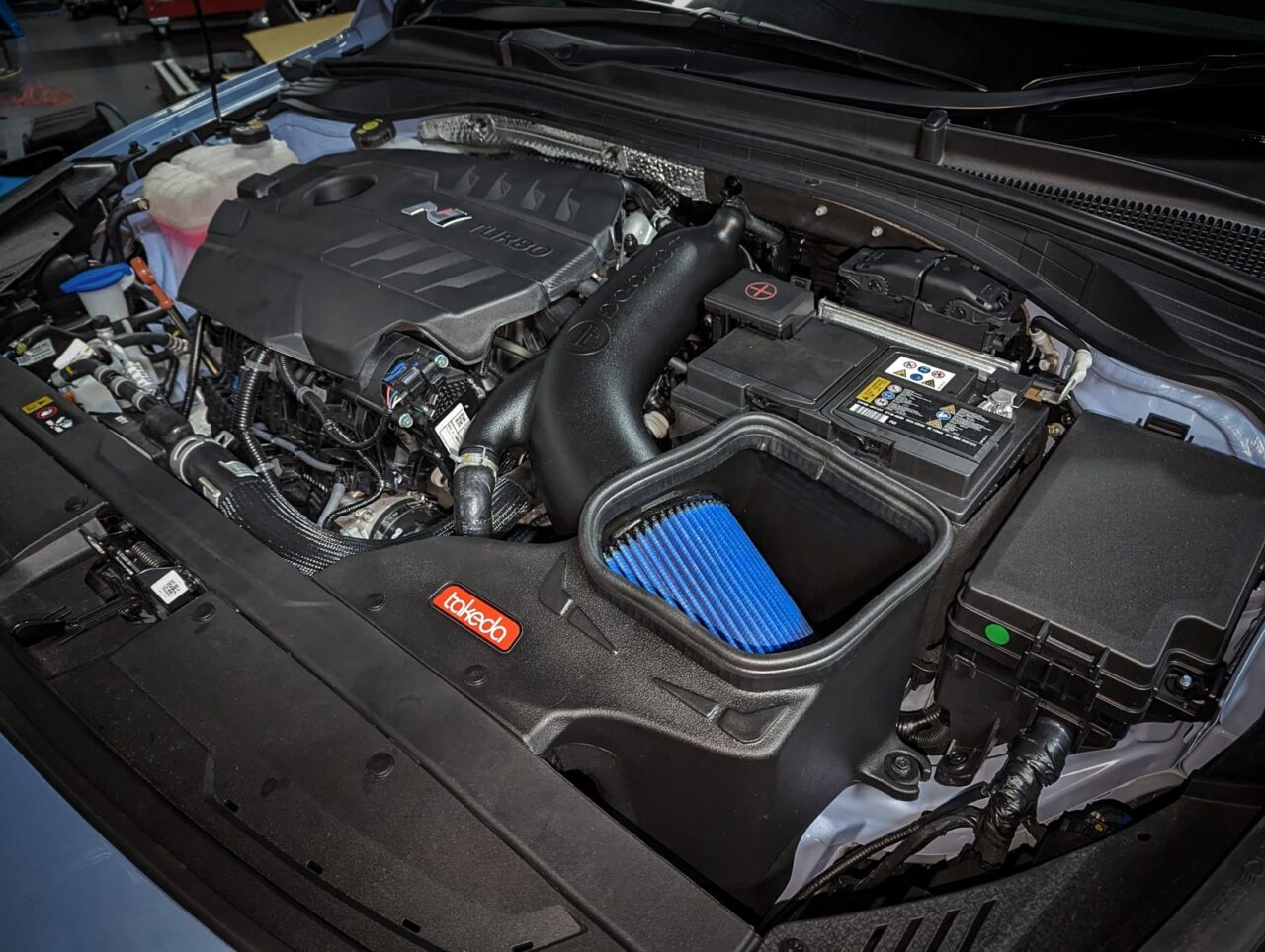 Aftermarket Takeda aFe brand cold air intake (CAI) with bright blue filter installed on Non-US Hyundai i30N engine bay