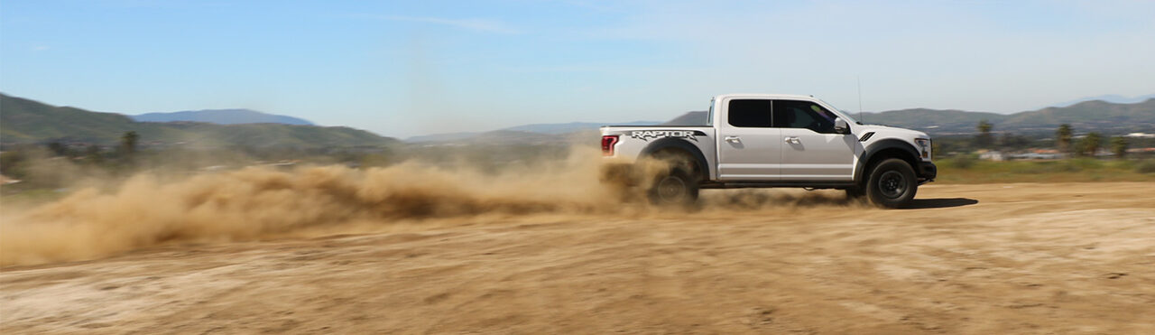 aFe POWER souped up with aftermarket performance parts White Ford Raptor driving fast in desert with huge dust trail in back