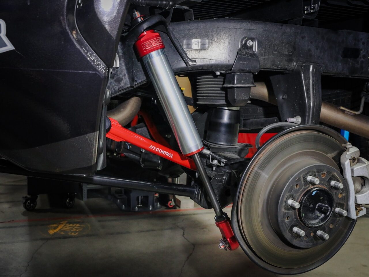 Closeup on aftermarket aluminum and zinc aFe POWER Sway-A-Way Rear Shocks with red accent and Red aftermarket AFE Control rear sway bar installed on 2022 Toyota Tundra wheel well