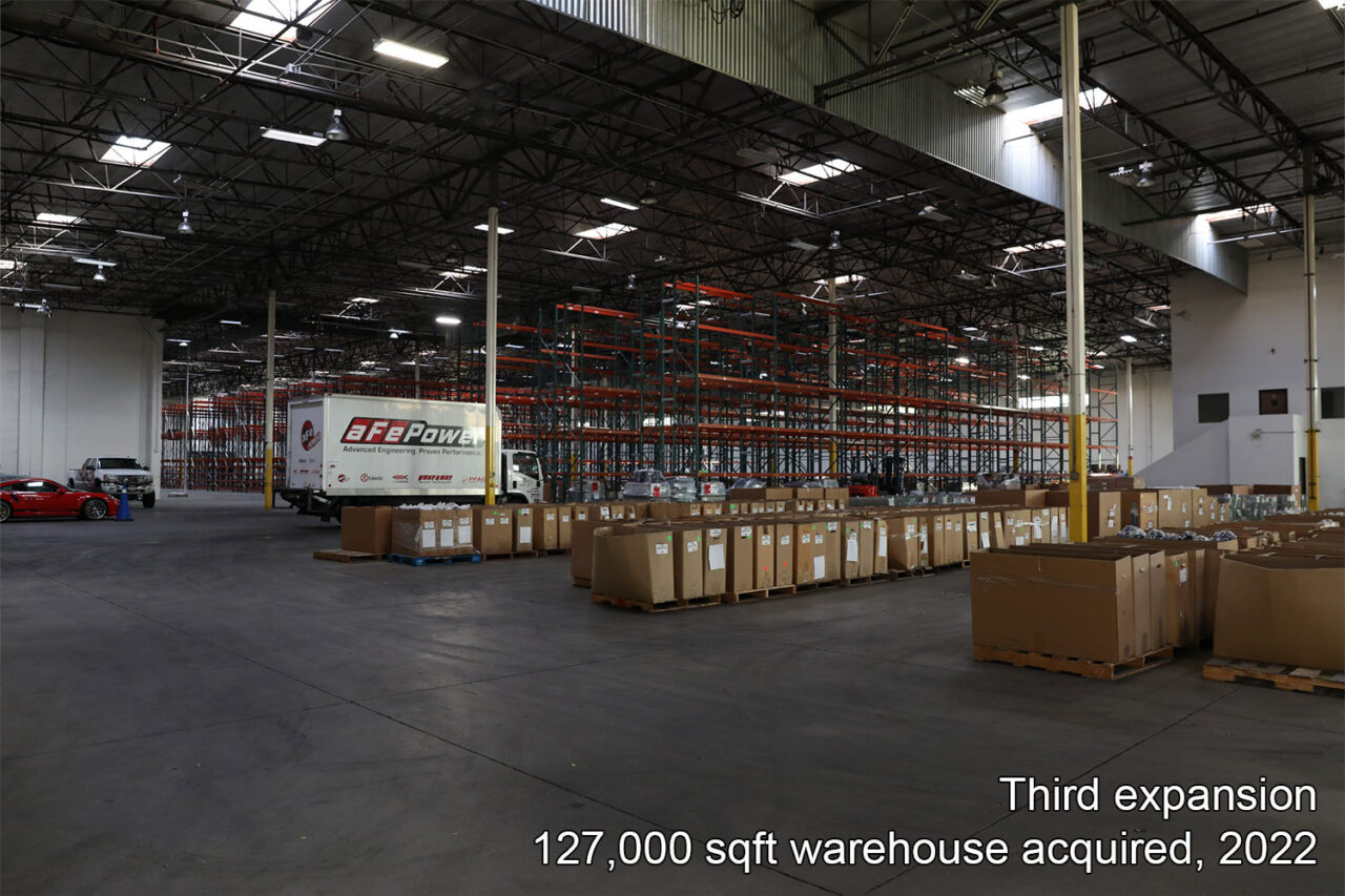 Inside of almost empty 127,000 sqft commercial building warehouse aFe POWER with boxes lined up of cold air intake manufactured in USA parts with aFe POWER box truck and more nice cars parked in background