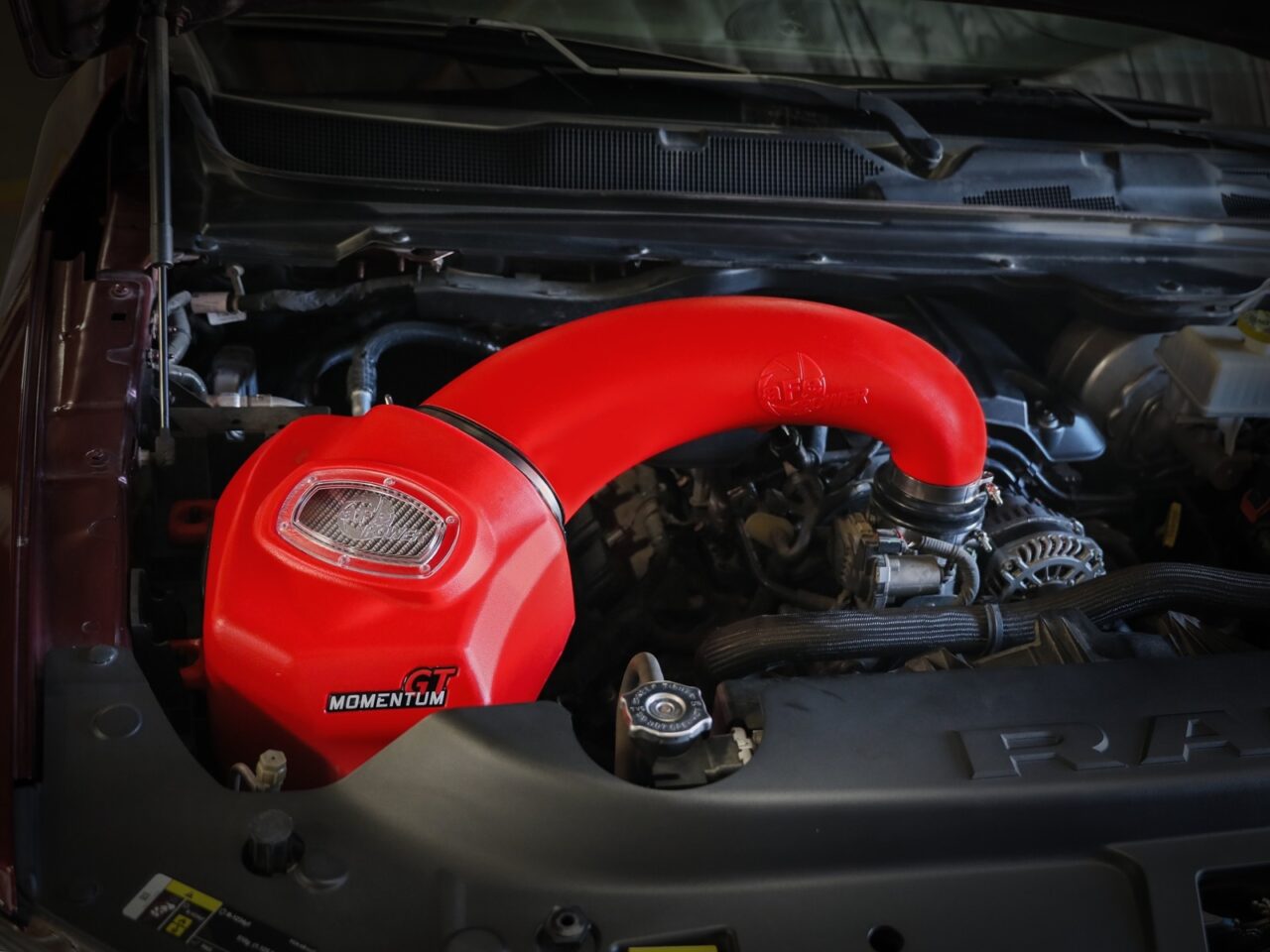 Bright red aftermarket AFE plastic aftermarket OE style airbox with red tube installed on RAM 1500 5.7L HEMI truck engine