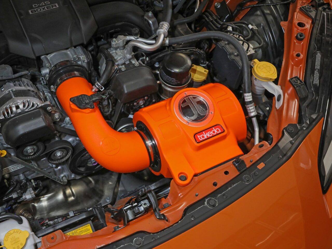 Bright orange plastic sealed Takeda intake with stylized window to filter installed on orange 2023 Toyota Gr86