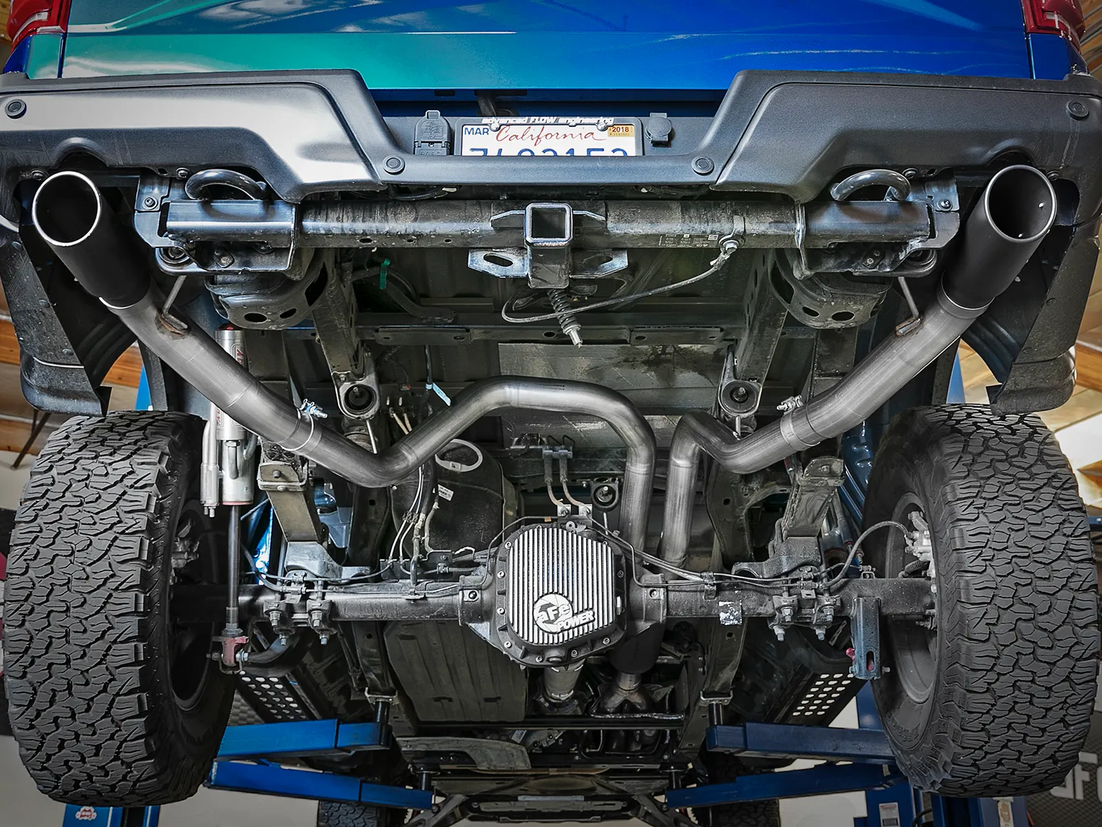 Under-shot of truck on lift showing aFe MACH Force Xp Cat-Back system with black exhaust tips installed on Blue Gen 2 F-150 Raptor and aFe Diff cover
