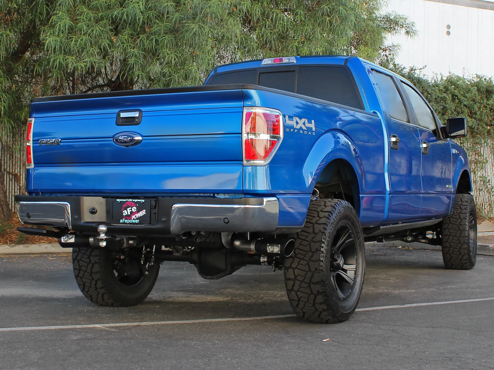 Rear angled view of 2011–2014 Ford F-150 3.5L EcoBoost in blue with aFe aftermarket cat-back exhaust system installed with dual large exhaust tips