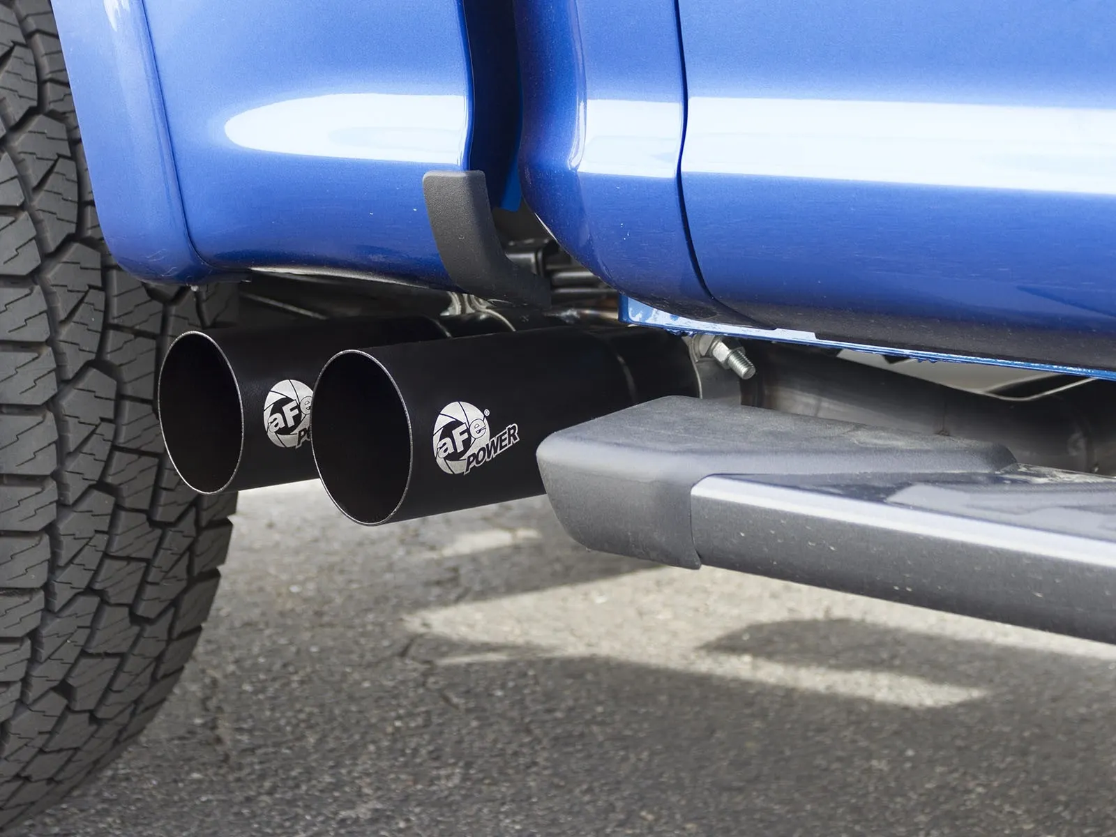 Close up of two black dual exhaust tips with aFe POWER logo right in front of passenger wheel of blue F-150 EcoBoost truck