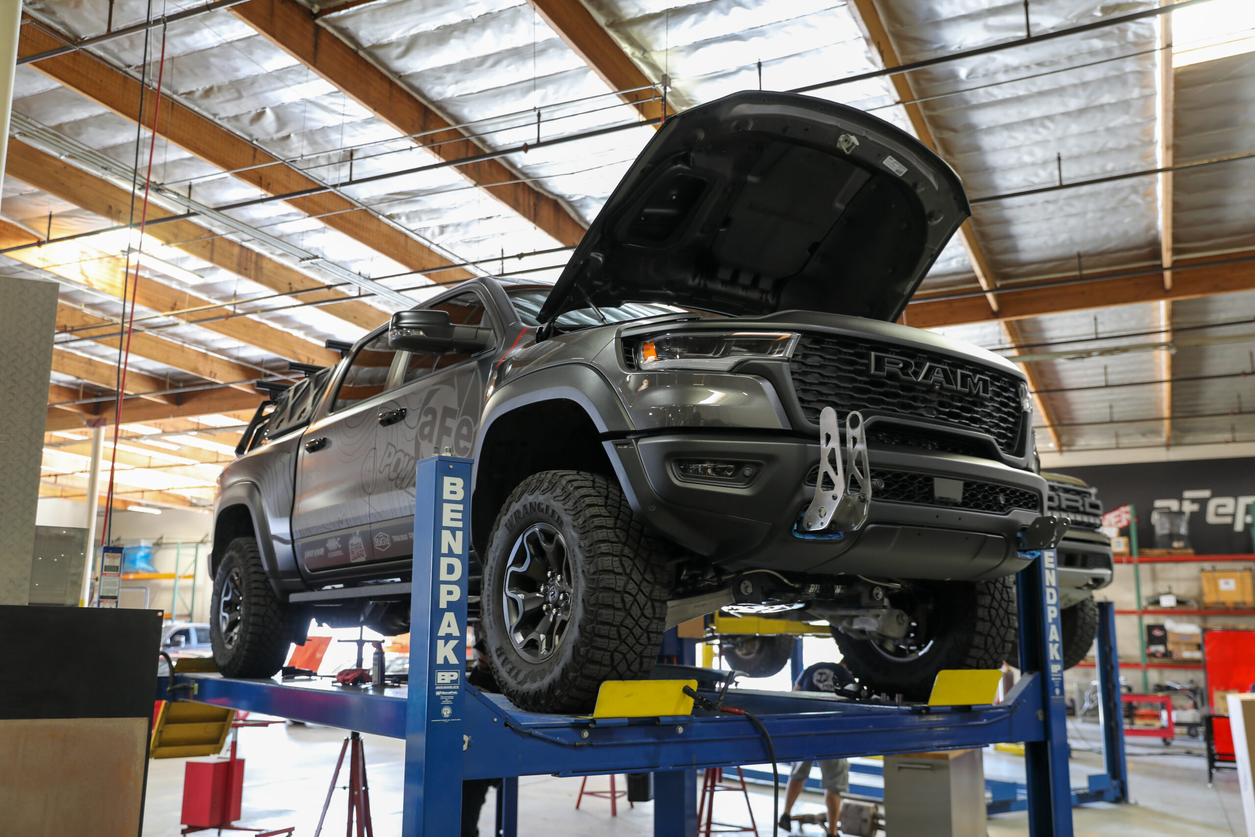 Front view of 2025 grey Ram 1500 RHO on lift in shop with hood open with bigger tires and off-road style build