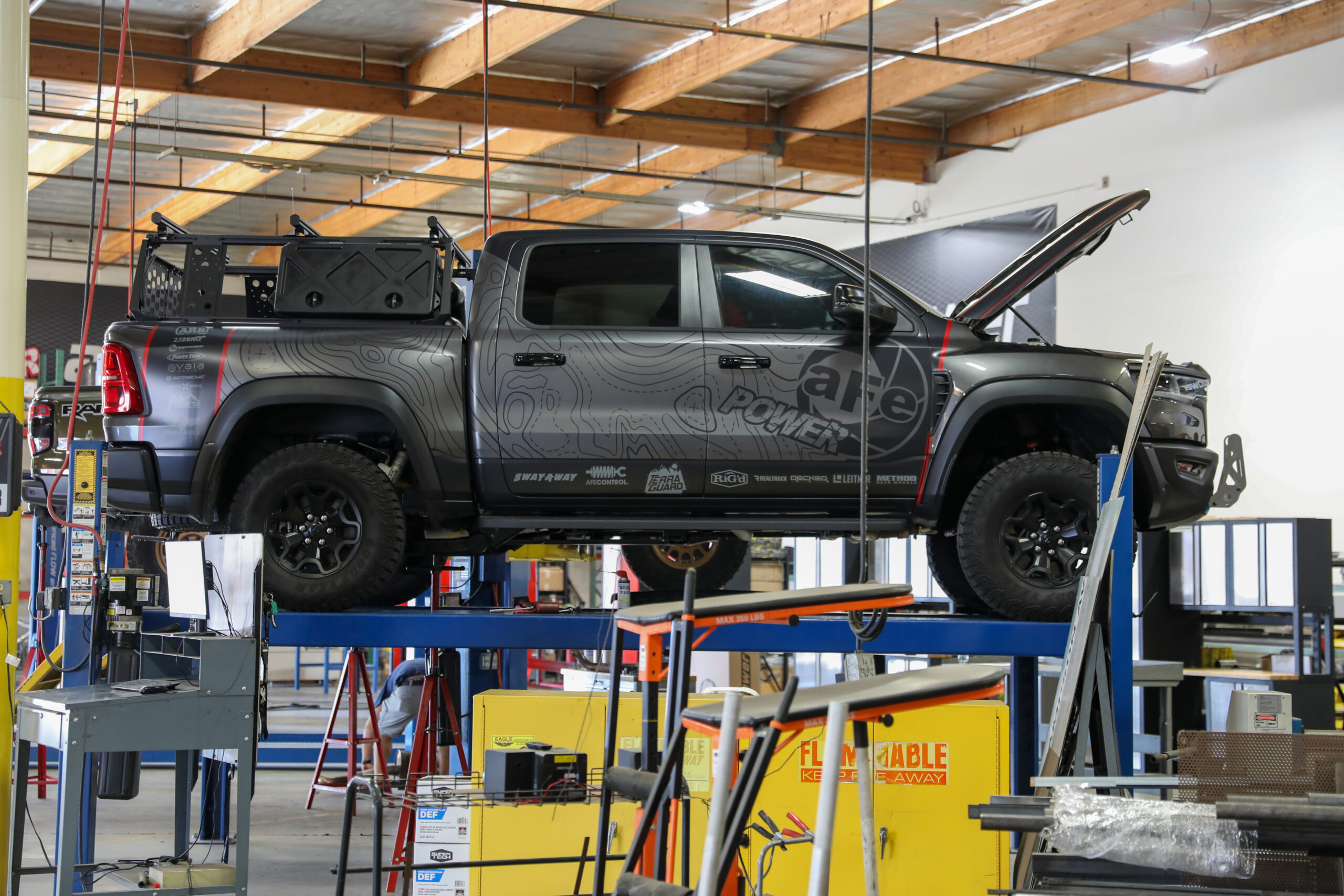 Grey RAM RHO truck with a wrap on a lift in a shop with bigger tires and overland style build
